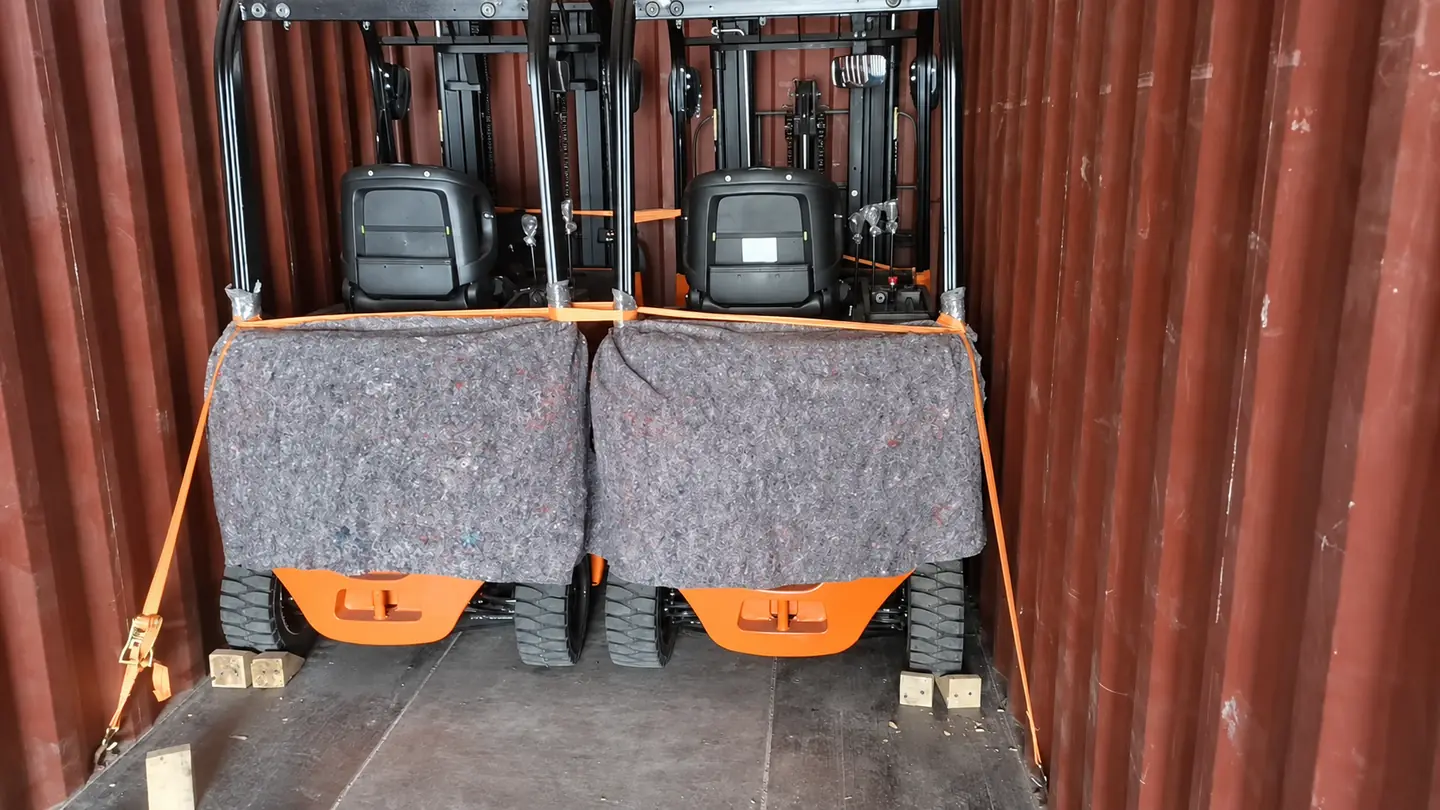 Two forklifts protected with blankets, straps and wheel chocks inside a shipping container