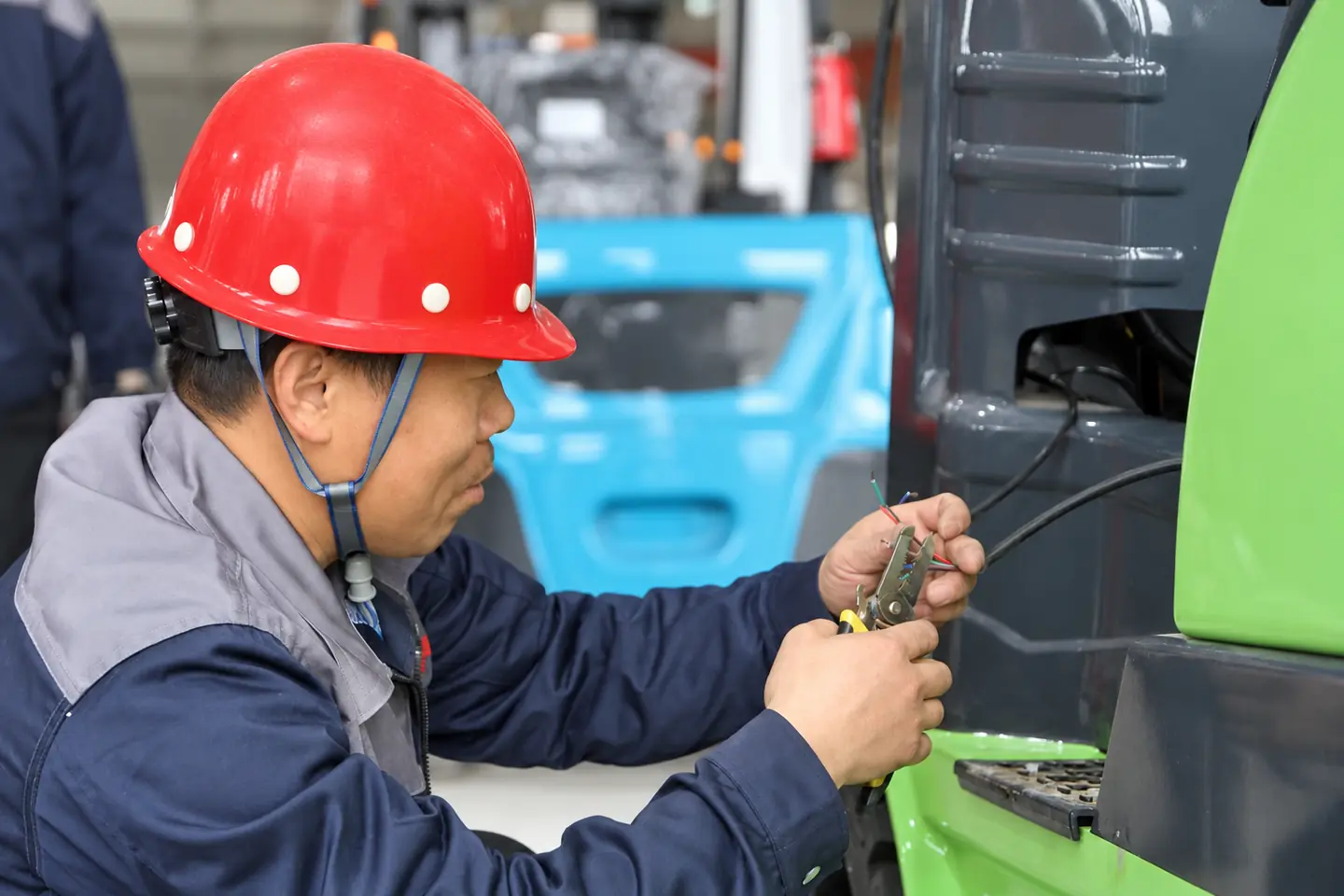 Workshop technician working on electrical wiring beside a green forklift