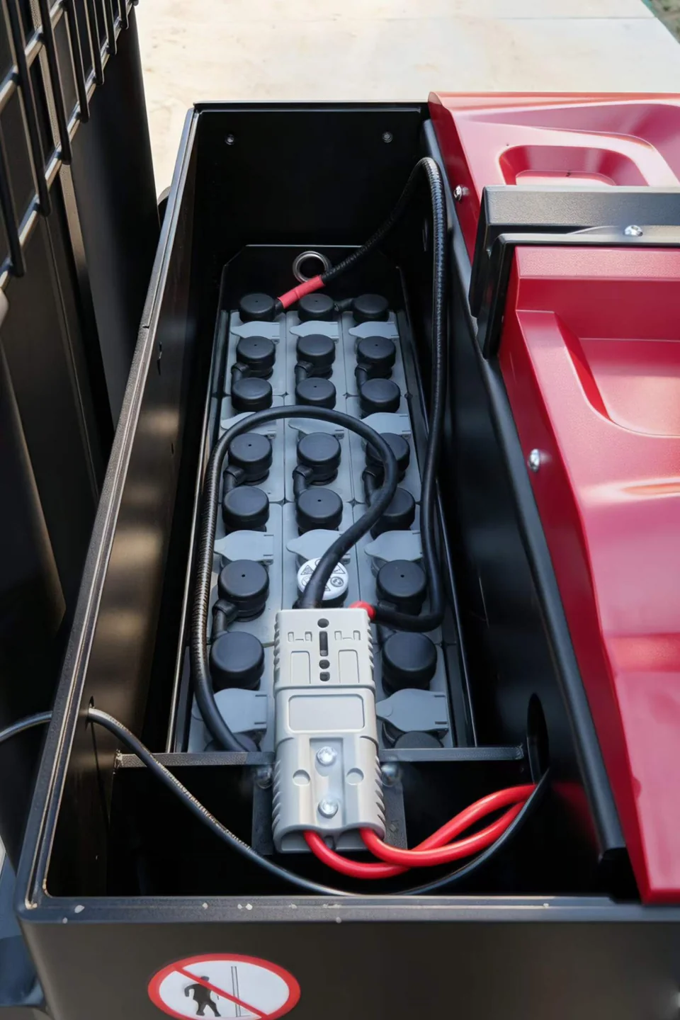 Electric stacker battery compartment showing individual cell caps, battery connector and cable routing