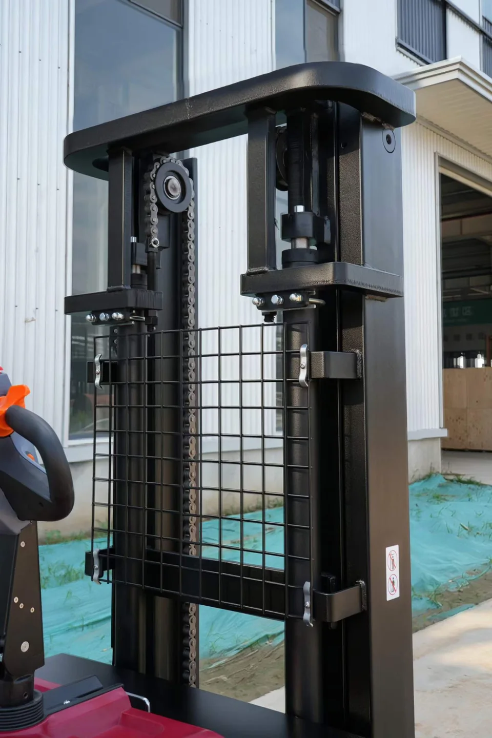 Electric stacker mast detail showing lift chains, mast rails, cylinders and protective mesh